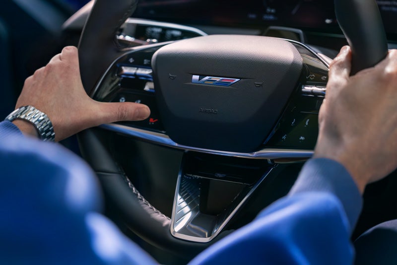 Close-up of a Man About to Press the V-Button on the 2026 OPTIQ-V Steering Wheel | Sheboygan Cadillac in Sheboygan WI